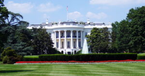 The White House, the official residence and workplace of the President of the United States, viewed from the front with a clear blue sky in the background.
